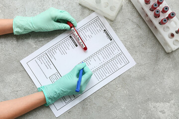 Doctor with HIV blood test tubes filling laboratory report form on grey grunge background