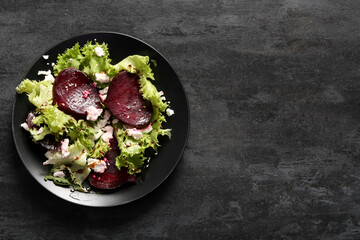 Plate of fresh salad with beet and cottage cheese on black background
