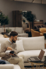 Obraz premium Man Working on Laptop While Sitting in a Modern Furnished Living Room