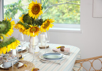Stylish dinnerware and sunflower in vases with burning candles on table