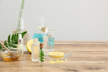 Laboratory glassware with ingredients and samples for preparing natural cosmetics on brown wooden table near white wall