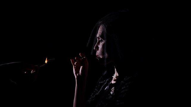 Retro woman actress silhouette with pin-up hairstyle and makeup isolated on black background, lights the mouthpiece and smokes. Slow motion.