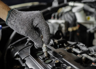 Male hand replacing spark plug in gasoline engine with engine compartment background. Car repair...