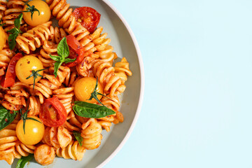 Plate of delicious fusilli pasta with tomatoes and basil on blue background