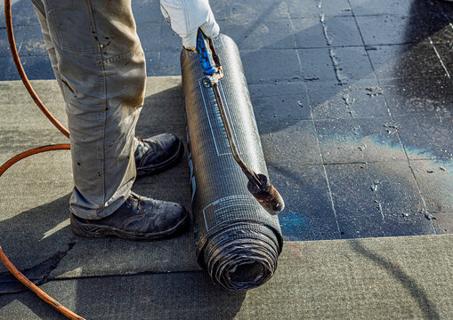 Roof waterproofing with bituminous membrane being installed. Close-up on the worker's feet and the membrane roll, showcasing the application process. Fata Morgana effect