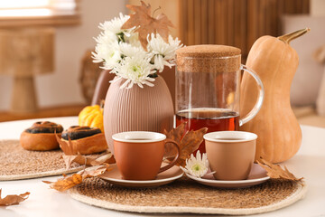 Cups of hot tea, tasty poppy buns, flowers and autumn leaves on table in living room
