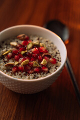quinoa porridge in a white bowl with pomegranate and nuts, vertical photo