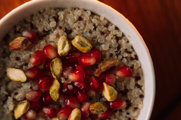 quinoa porridge in a white bowl with pomegranate and nuts, top view, close up