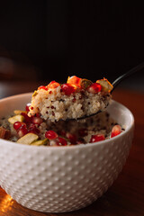 quinoa porridge in a white bowl on spoon with pomegranate and nuts
