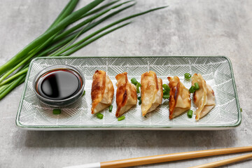 Plate with fried Japanese gyoza, green onion and bowl of soy sauce on grey background