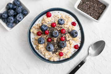 Bowl with tasty oatmeal, chia seeds and berries on white background