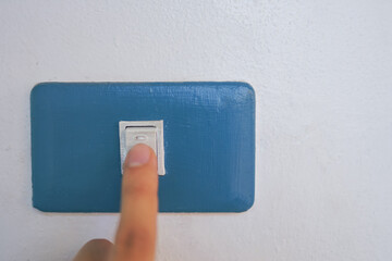 Hand holding a light switch on the wall with a smartphone nearby