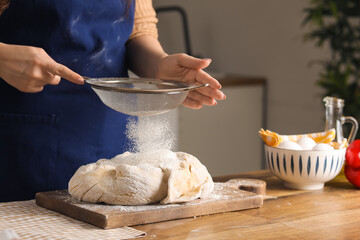 Woman with sieve sprinkling flour on fresh dough in kitchen