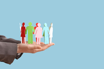 Female hands with paper human figures against color background. Diversity and inclusion concept