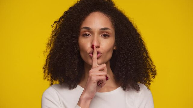 Woman making shushing gesture for silence on yellow background