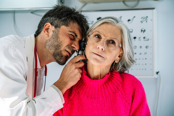 Doctor examining senior woman's ear with otoscope in medical clinic