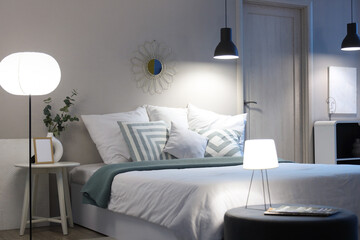 Interior of modern bedroom with cozy bed, houseplants and glowing lamps at night