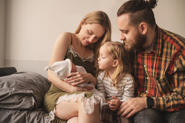 Happy family meets new baby. Mom, dad, older daughter and newborn son. Parents introduce older...