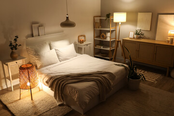 Interior of stylish bedroom with cozy bed and glowing lamps at night