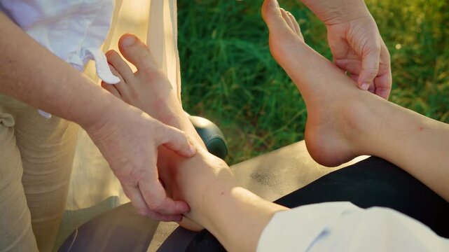 Therapist massaging foot of patient. Specialist kneading ankle of client under tree shade. Master pressing sole of patient in outdoor setting. Practitioner rubbing foot of client near greenery