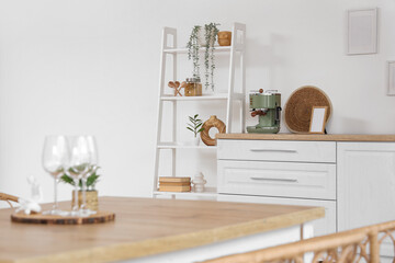 Glasses, figure and houseplant on dining table in light kitchen, closeup