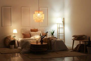 Interior of stylish bedroom with cozy bed, houseplants and glowing lamps at night