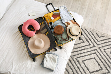 Unpacked suitcase with clothes and travelling accessories on bed in hotel room