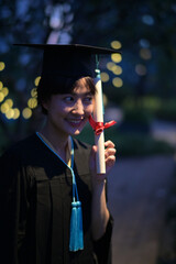 joyful asian woman graduate holding diploma with red ribbon in low light setting, surrounded by...