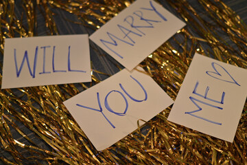 Proposal message written on cards with golden tinsel background, creating romantic and celebratory...