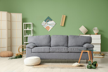 Interior of messy living room with grey sofa, coffee table and overturned houseplant after...