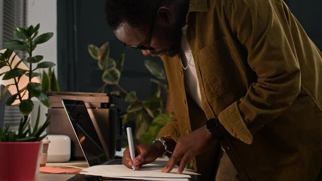 Mid-section of young African American male employee in casualwear signing contract before making copies on printer at desk with wireless laptop at startup office