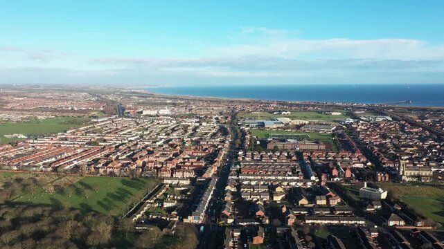 Aerial drone footage of the town of Hartlepool in the UK showing rows of terrace houses and homes with the ocean and harbour in the background on a sunny day in the winter time