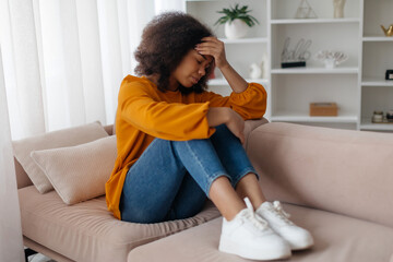 Depressed young black woman suffering from headache, pressing her forehead with grimace of pain,...