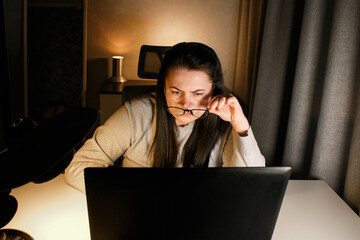 Woman working on computer late evening at home office. Concentrated female freelancer trying to...