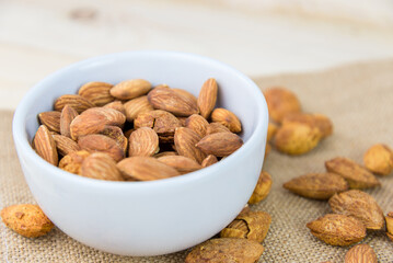 Almonds and almond dry food in white bowl on sack and wooden table background. Almond concept with copyspace. Almond is snack or raw of cook. Healthy food.