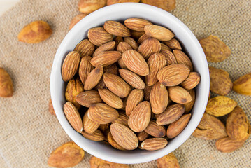 Almonds and almond dry food in white bowl on sack and wooden table background. Almond concept with copyspace. Almond is snack or raw of cook. Healthy food.