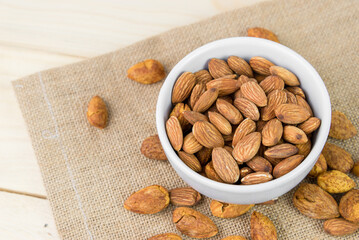 Almonds and almond dry food in white bowl on sack and wooden table background. Almond concept with copyspace. Almond is snack or raw of cook. Healthy food.
