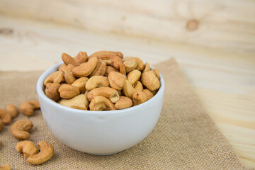 Roasted cashew nut in the white bowl on sack background. Cashew nut is snack or raw of cook. Healthy food. Low calories or diet food. cashew nut with copyspace.