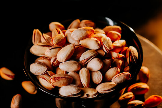 Delicious pistachios displayed in a black bowl under warm lighting, perfect for snacking or cooking
