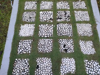 Grid pattern of green grass and white gravel squares. Ground texture or landscaping detail