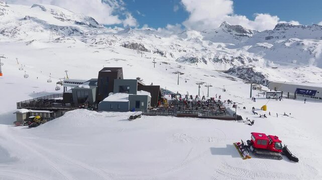 Aerial view of Cervino Ski Paradise resort with skiers, snowboarders, a red snow groomer in motion, and ski lifts near the Matterhorn mountain.