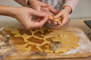 close-up, hands of mother and little child cutting cookies of raw gingerbread dough in kitchen, Christmas traditions