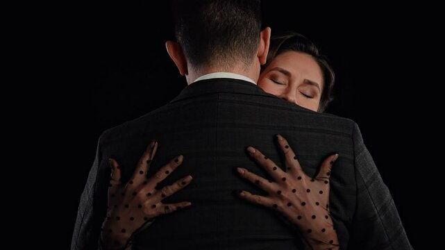 Retro woman actress with pin-up hairstyle and makeup isolated on black background, woman hugging and kissing man, smiling looking at camera. Slow motion.