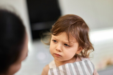 offended little child girl in striped apron talks to mom in kitchen, mom forbade something to her...