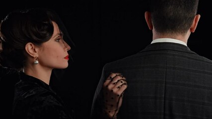 Retro woman actress with pin-up hairstyle and makeup isolated on black background, woman in veil touching man on the back and looks at camera. Slow motion.
