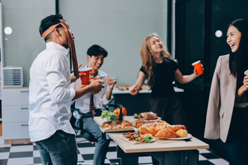 Asian office colleagues and friends enjoy a daytime BBQ with pizza and beer, celebrating Halloween and cheering for their favorite soccer team, creating a lively atmosphere filled with joy.