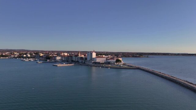 Scenic drone shot of the coastal town of Umag, Croatia, showcasing the marina, harbor wall, and historic town center beside the Adriatic Sea. 