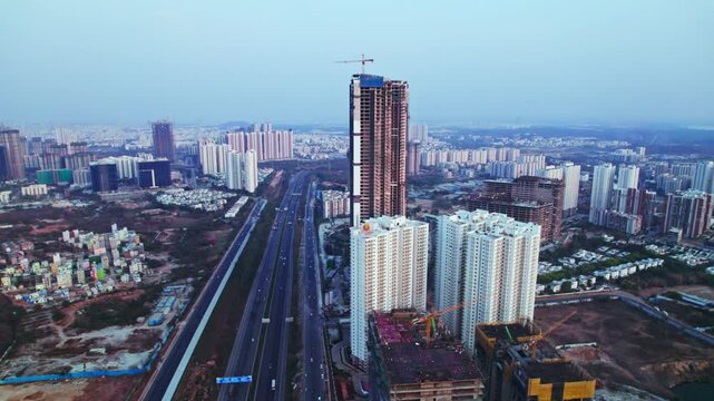 Tallest under construction building with crane construction and outer ring road at financial district, nanakramguda, hyderabad, telangana, india. day time, pan shot, drone shot, 4k.