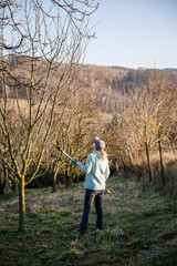 Female farmer trimming tree using telescopic pruning shears in orchard. Woman at work. Spring...