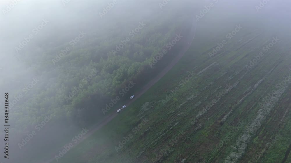Poster watch as drone soars through low clouds, capturing a car overtaking another with trailer on a rustic